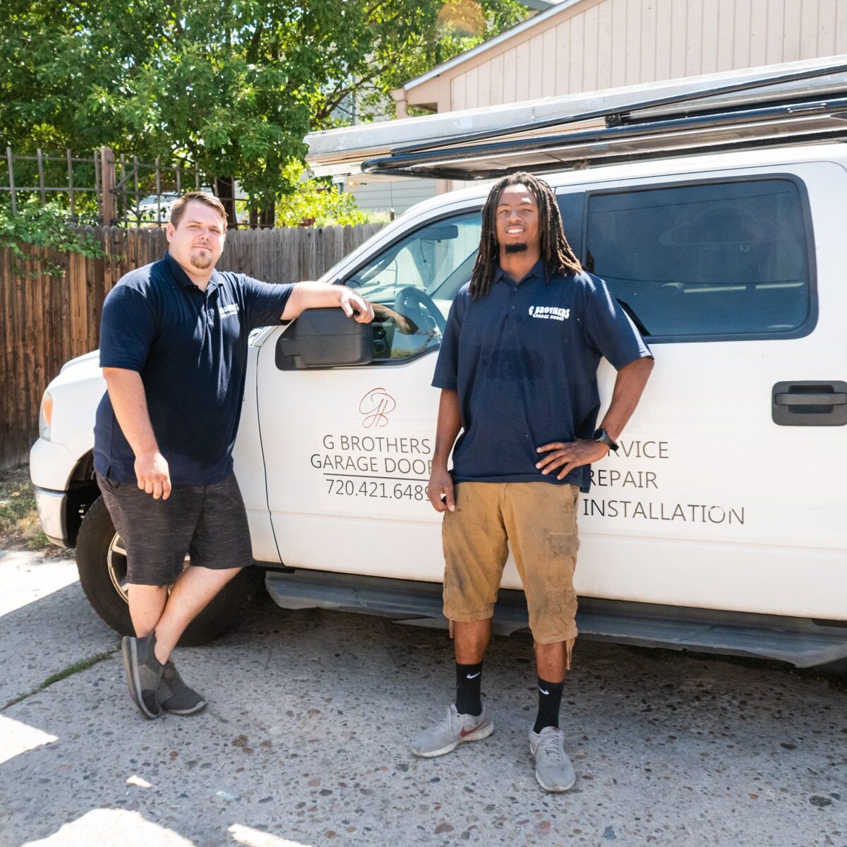 Two G Brothers garage door technicians standing beside a branded G Brothers service truck in Lakewood