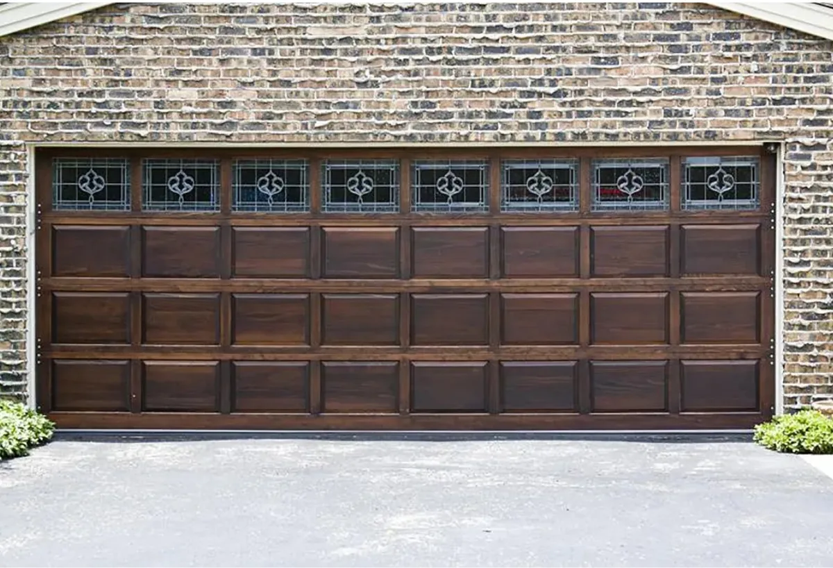 A rich wood carriage-house garage door with decorative glass on a brick home, a curb-appeal upgrade